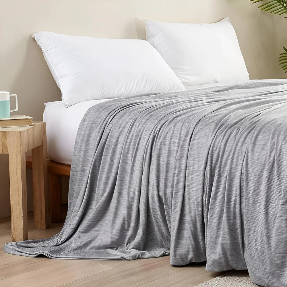 White cooling blanket with 400 thread count displayed on a grey bed frame, accompanied by pillows, set on a wooden floor.