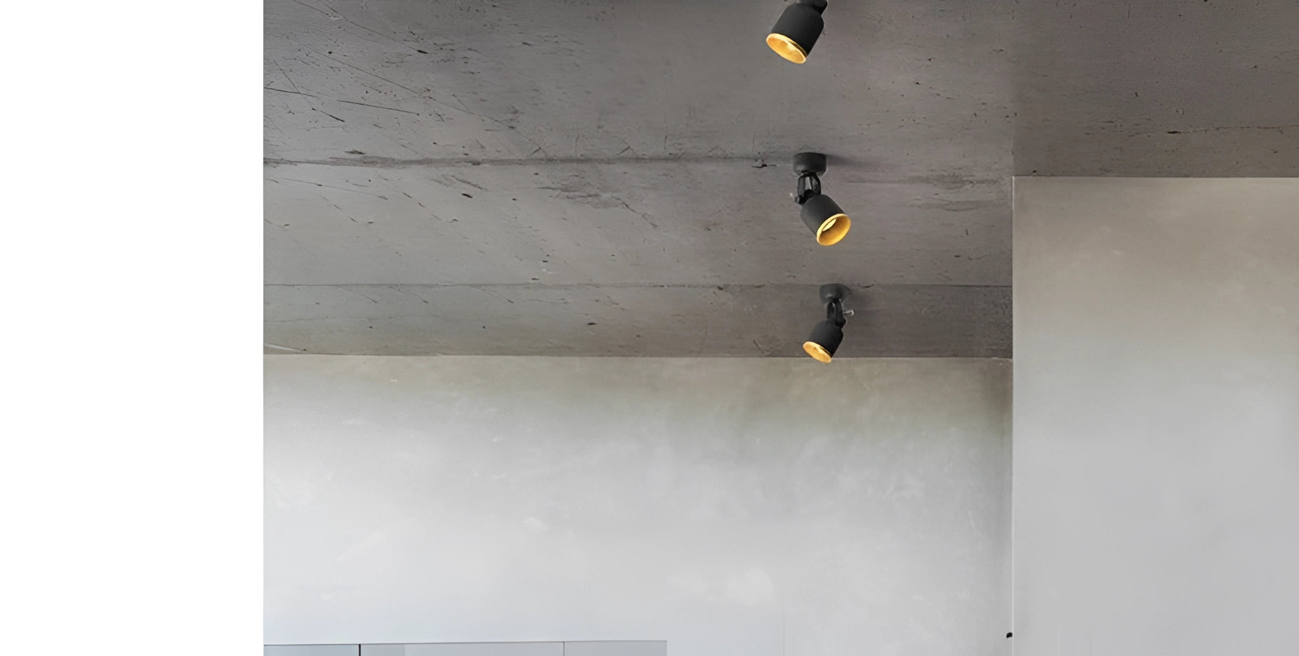 Adjustable black and gold LED track light mounted on a modern ceiling, with its sleek, rectangular design providing focused illumination. The ceiling appears to have a grey and concrete-like texture, complementing the contemporary aesthetic.