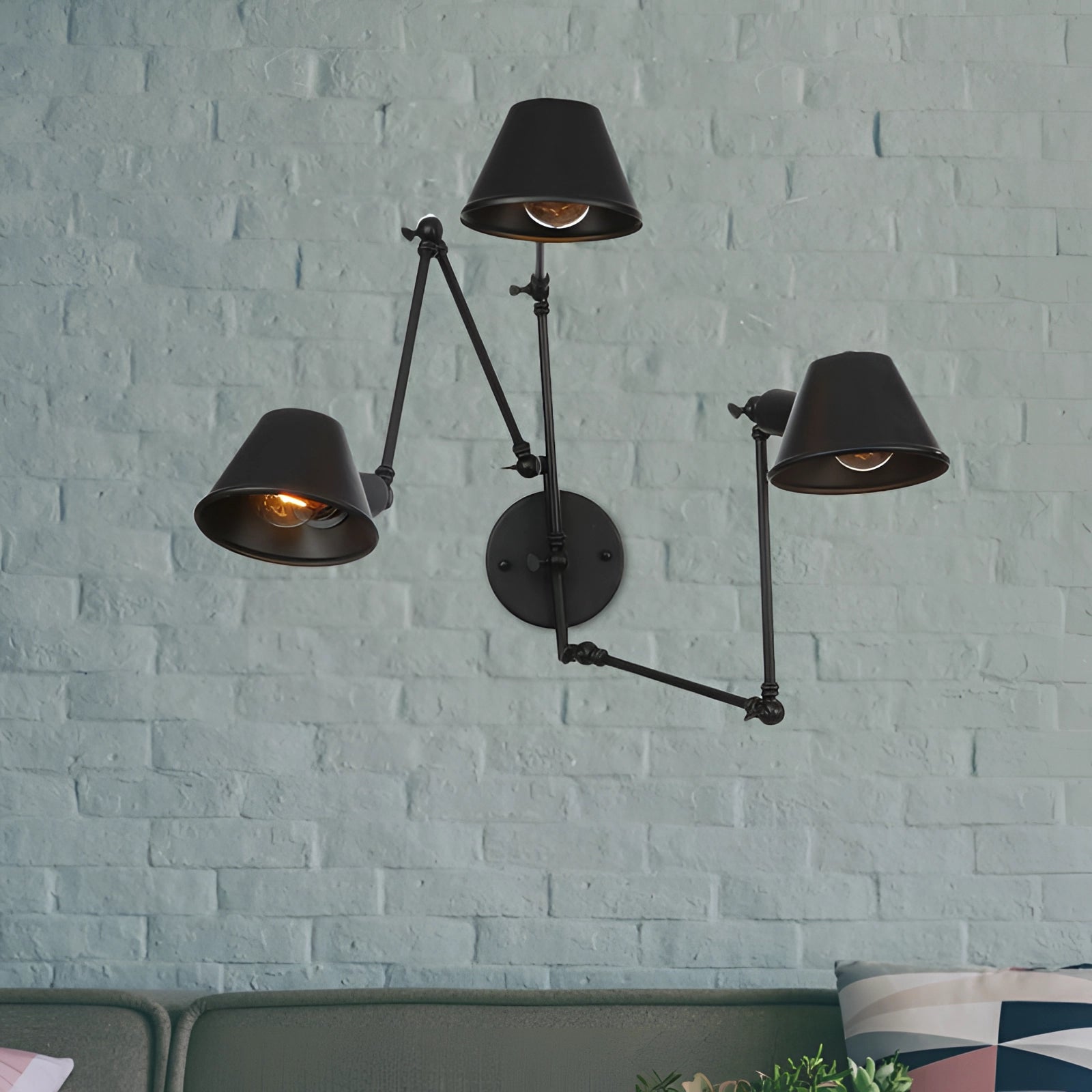 Adjustable triple-arm black wall sconce with modern industrial design features, mounted on a grey wall above wooden shelving adorned with plants.