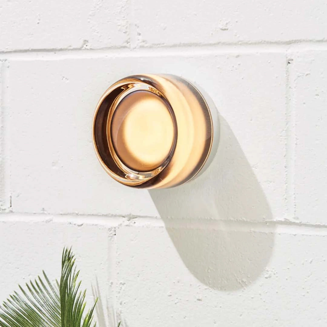 Modern minimalistic round amber glass ceiling light fixture with wooden accents, mounted on a beige ceiling above a doorway, surrounded by indoor plants.