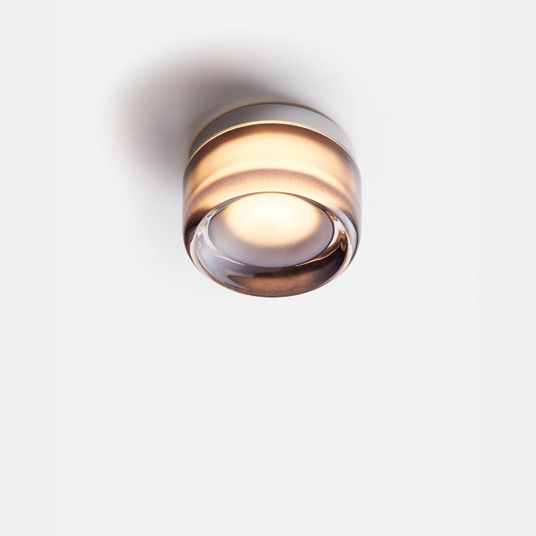 Modern minimalistic round amber glass ceiling light with gray finish, featuring a circular design made of metal and glass elements.