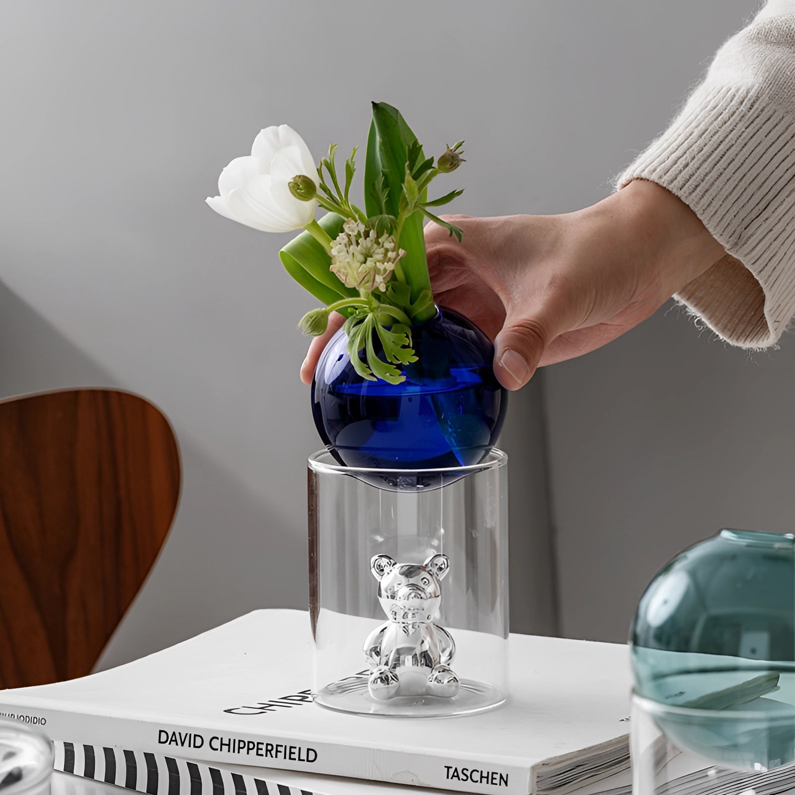 A luxurious decor capsule featuring a gold bear figurine and an amber glass sphere, styled with a houseplant in a vase on a table, adding elegance and sophistication to the setting.