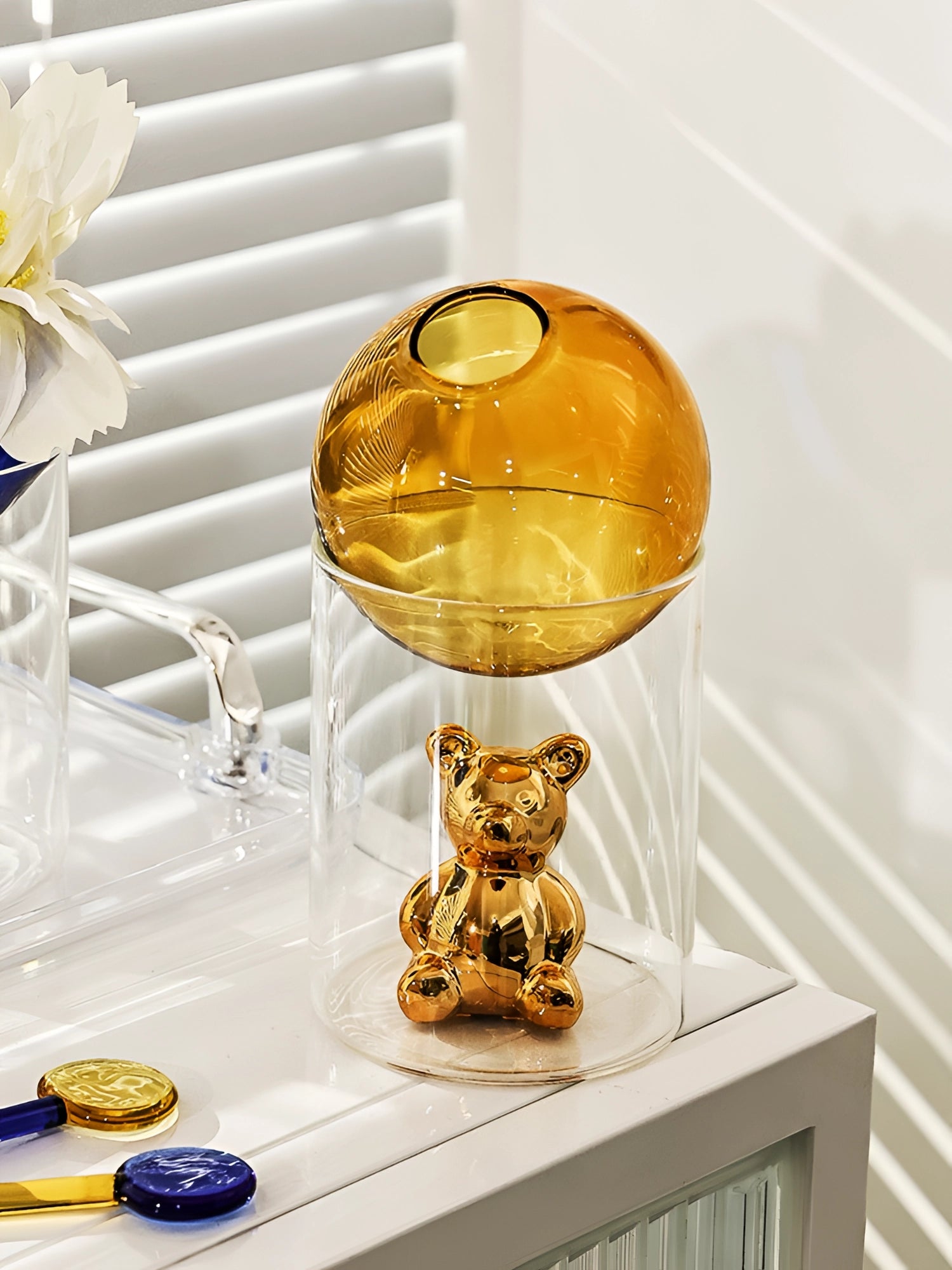 Amber glass sphere paired with a gold bear figurine, elegantly displayed as a luxury decor piece, featuring warm hues of amber, orange, and yellow, accentuated by artistic plant-like elements.