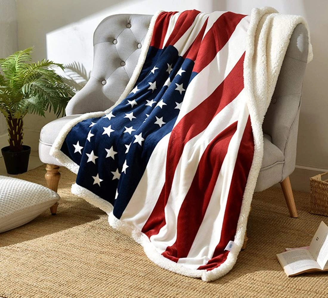 American flag fleece blanket with a stars and stripes pattern draped over a sofa armrest, surrounded by houseplants in flowerpots.