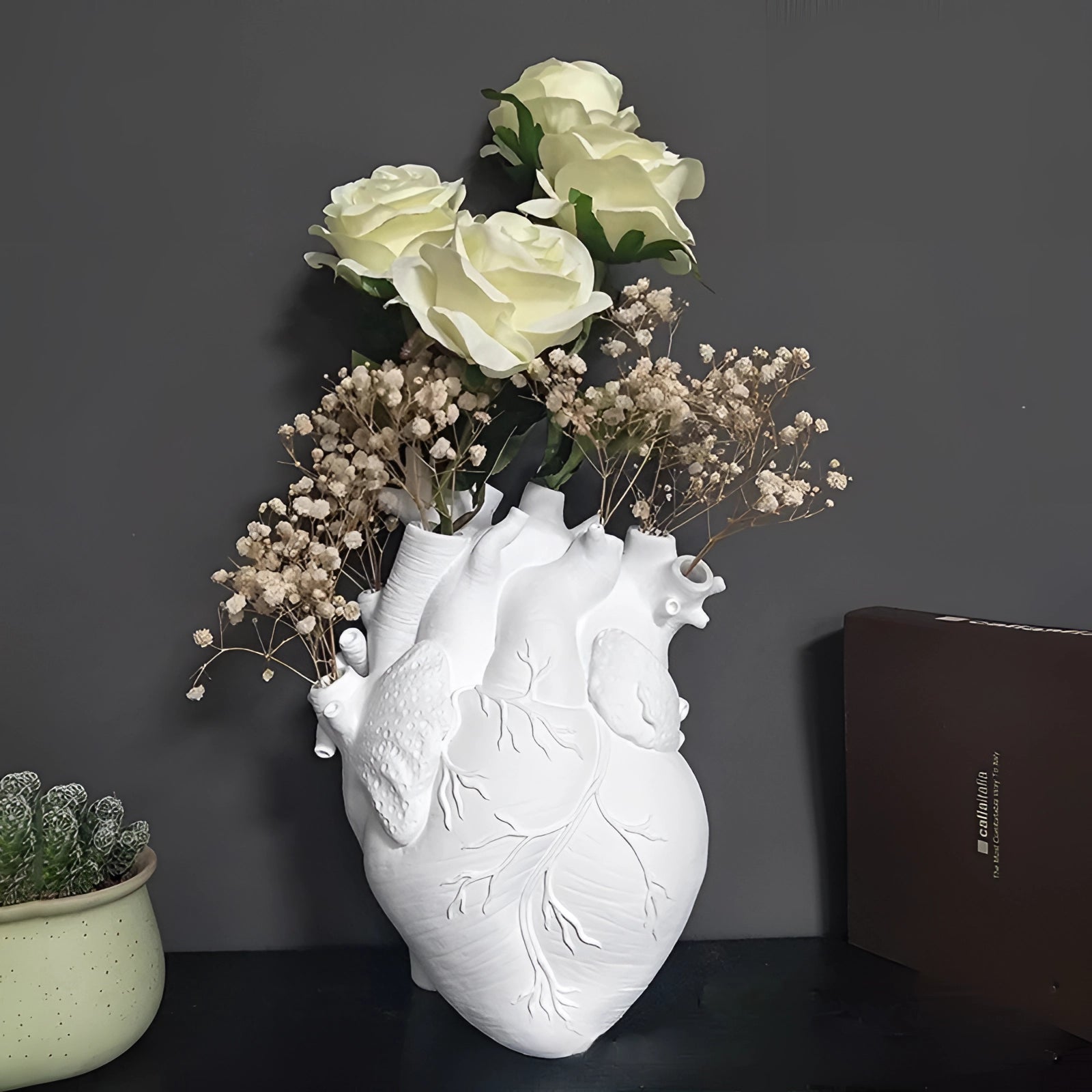 An artistic heart-shaped vase designed to resemble an anatomical heart, creatively used as a flower planter, displaying an arrangement of colorful flowers and green plants.