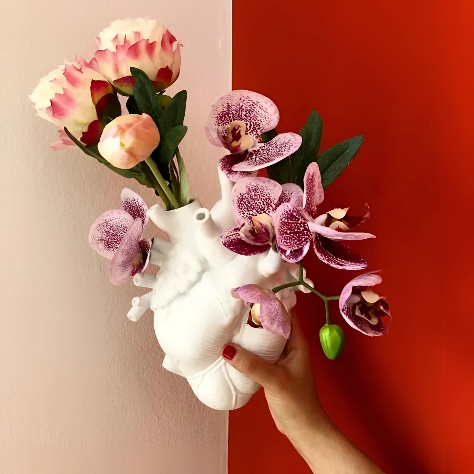 Anatomical heart-shaped vase used as a creative and artistic flower planter decor, featuring a detailed arrangement of colorful artificial flowers and petals.