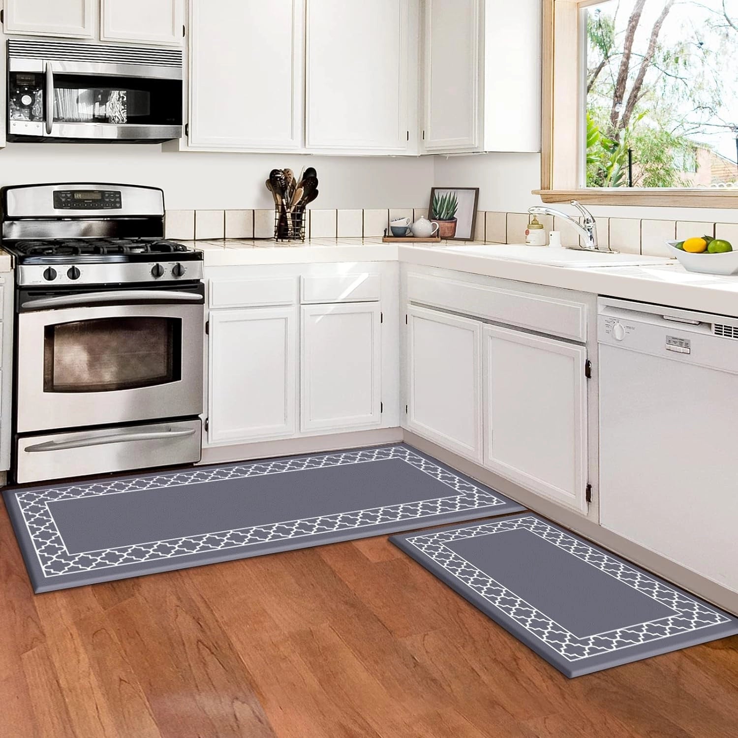 Anti-fatigue cushioned kitchen mat in grey, shown as a set of two sizes (50x80cm and 50x120cm), placed in a modern kitchen setting with white cabinetry and countertop, near a kitchen sink and stove. The mat is designed to be ergonomic and slip-resistant, providing comfort and stability while standing in the kitchen.