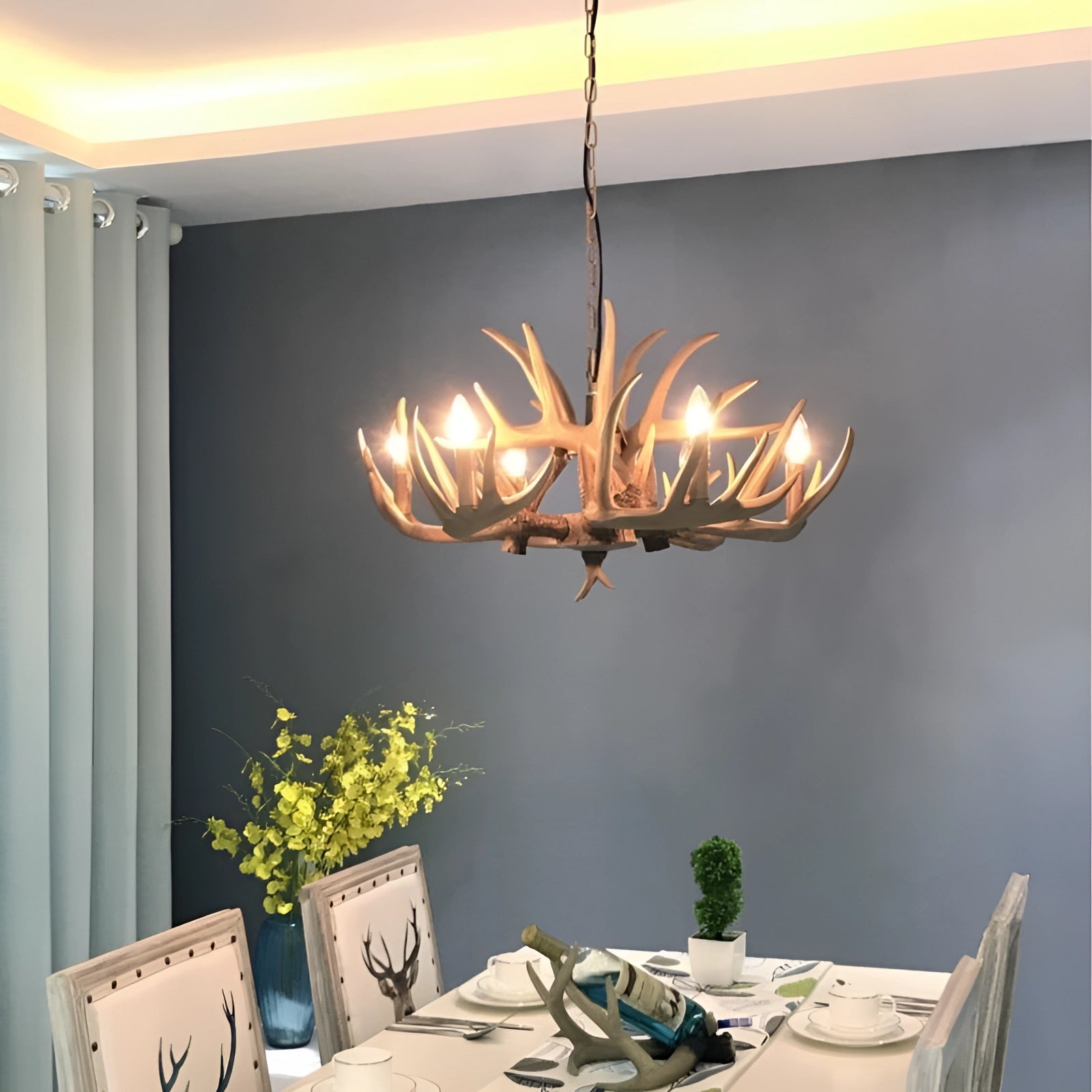 Antler chandelier hanging in a rustic lodge-style interior with wooden accents and decorative elements, such as plants and tableware, creating a cozy cabin atmosphere.