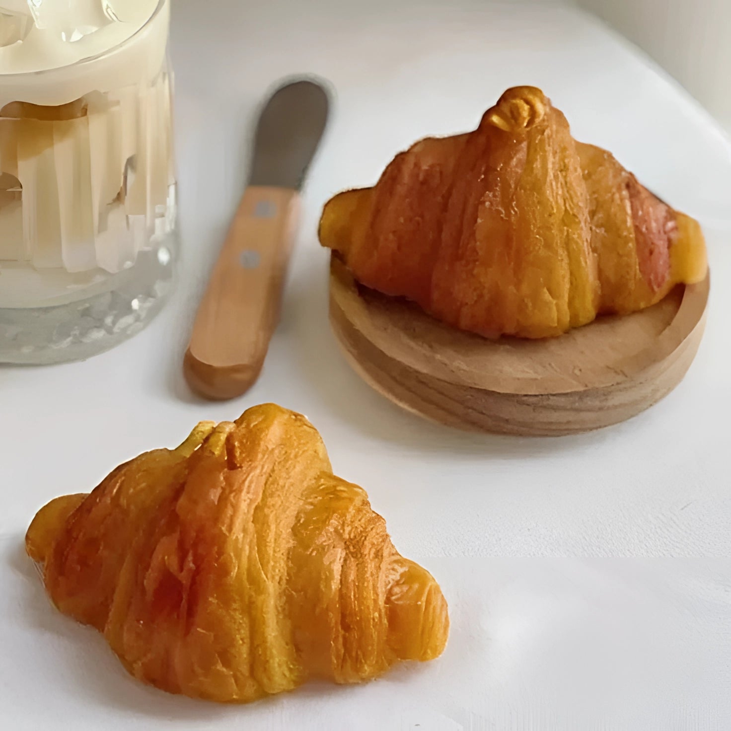 Artisan croissant on a wooden table, showcasing its golden, flaky layers, surrounded by a few rustic tableware items.