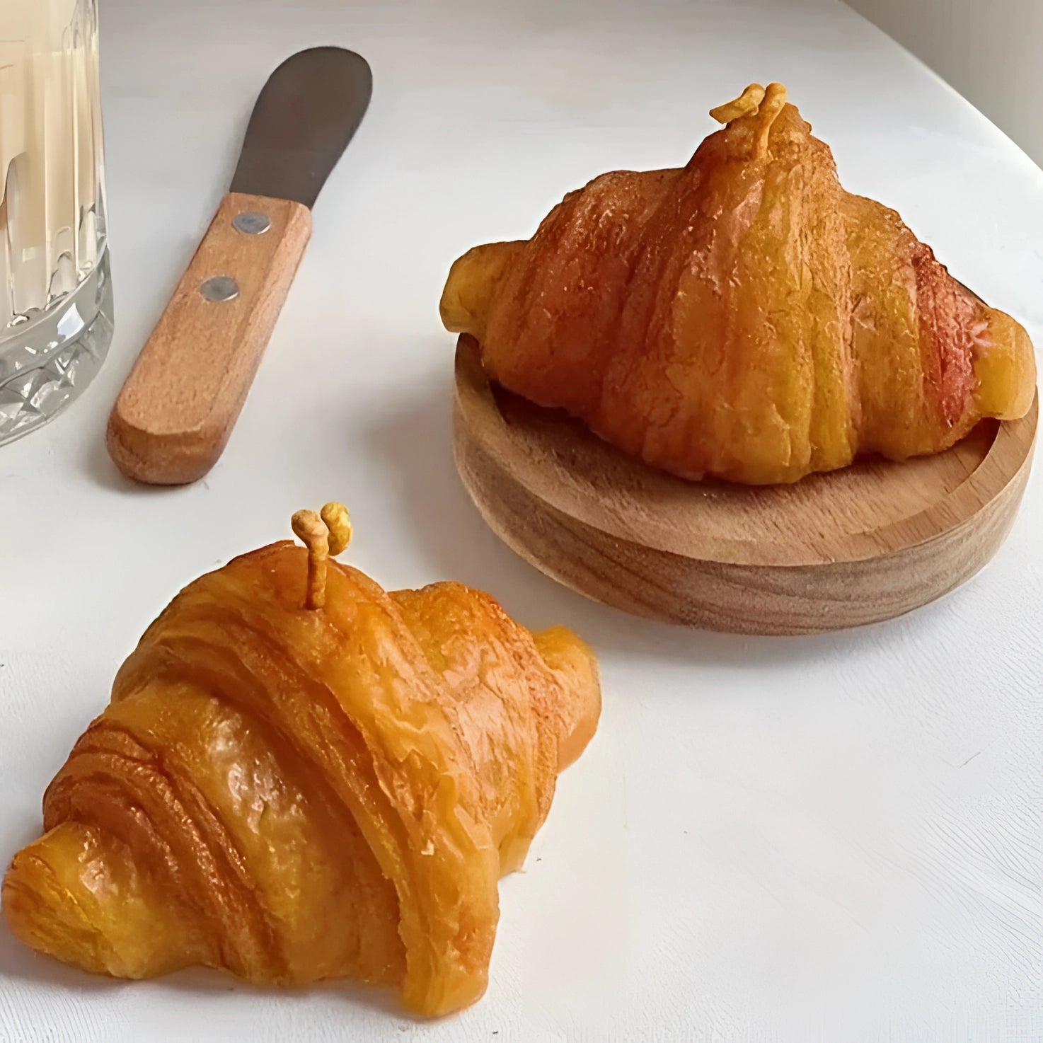 Flaky artisan croissant served on a white plate, placed on a wooden table, showcasing its golden-brown, layered exterior.