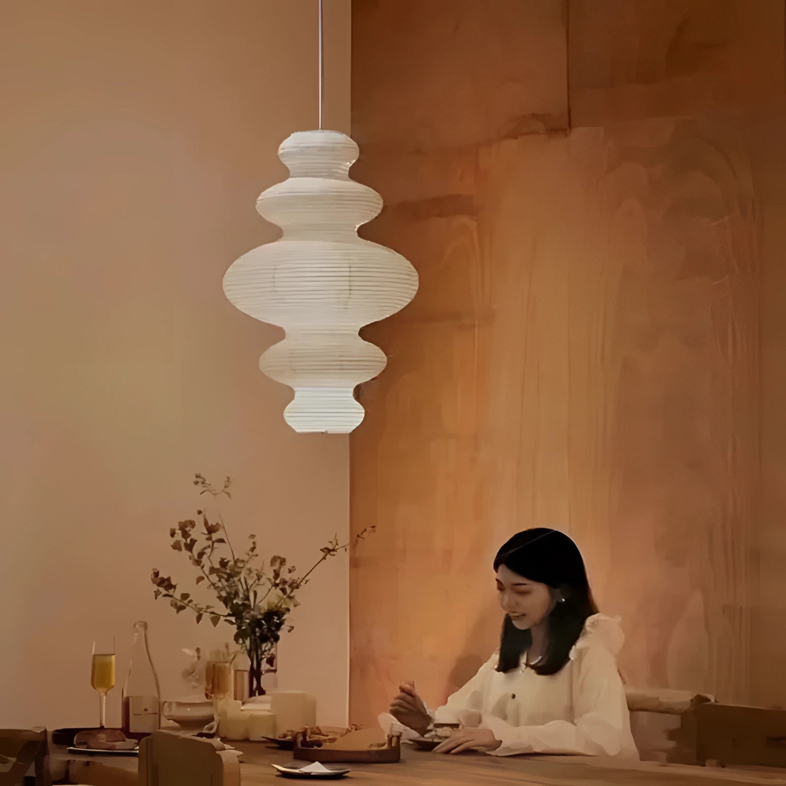 Asian-inspired pendant light made from rice paper and natural fibers, featuring a soft, warm glow and organic texture, hanging from the ceiling above a wooden table.