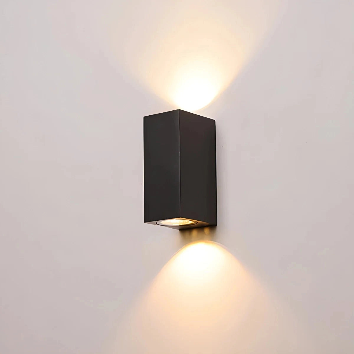 Modern Black LED Cylindrical Outdoor Wall Lamp in Sand Black Finish, Square Shape, Mounted on Wooden Surface, Illuminated with Warm Amber Light.