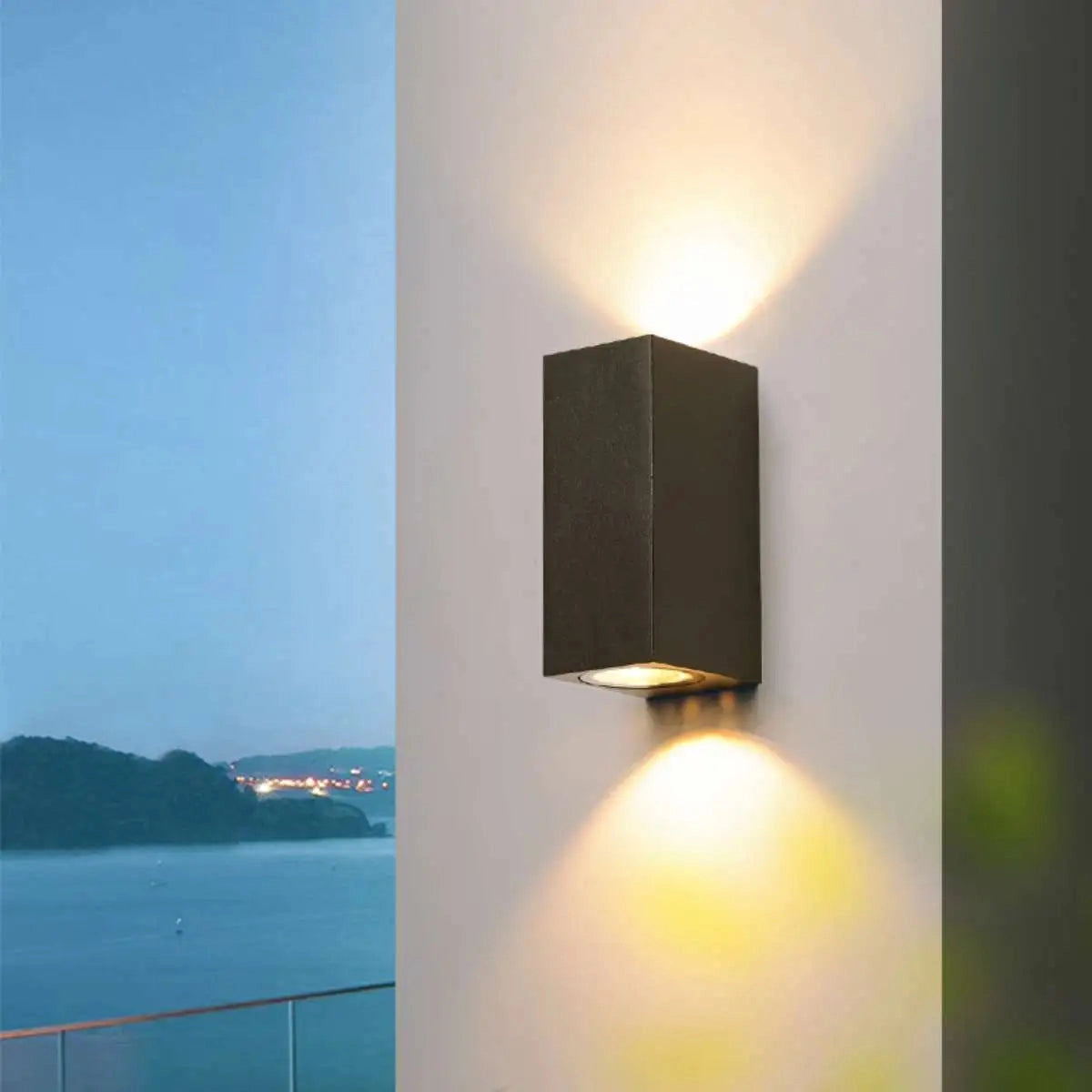 Modern black cylindrical LED outdoor wall lamp mounted on a wooden exterior wall, glowing warmly against a dusky sky.