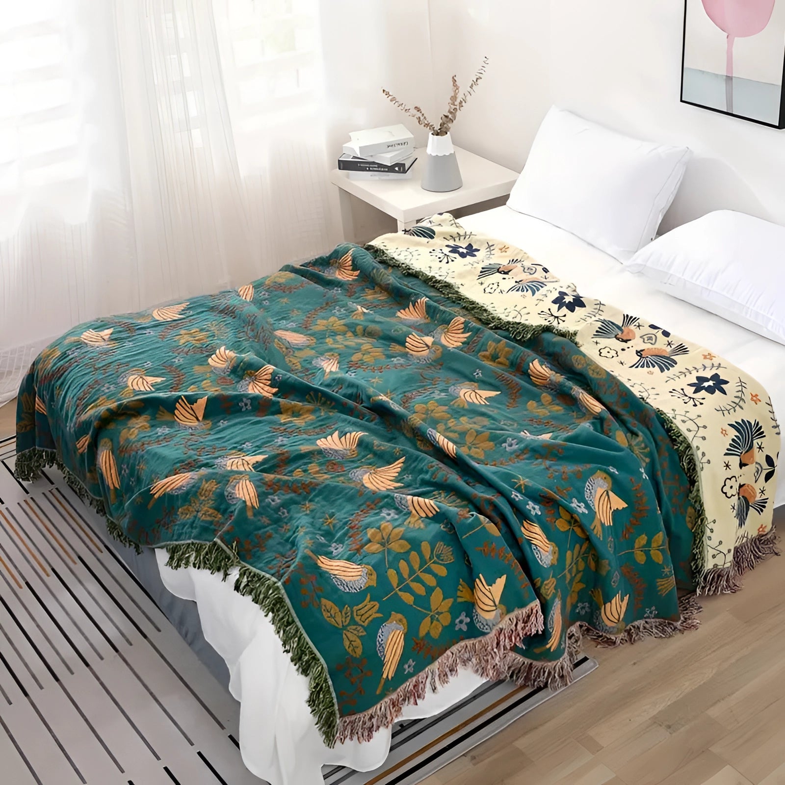 Bohemian Bird Pattern Throw Blanket in blue and beige with fringed edges, draped over a bed in a cozy interior setting featuring pillows and wooden flooring.