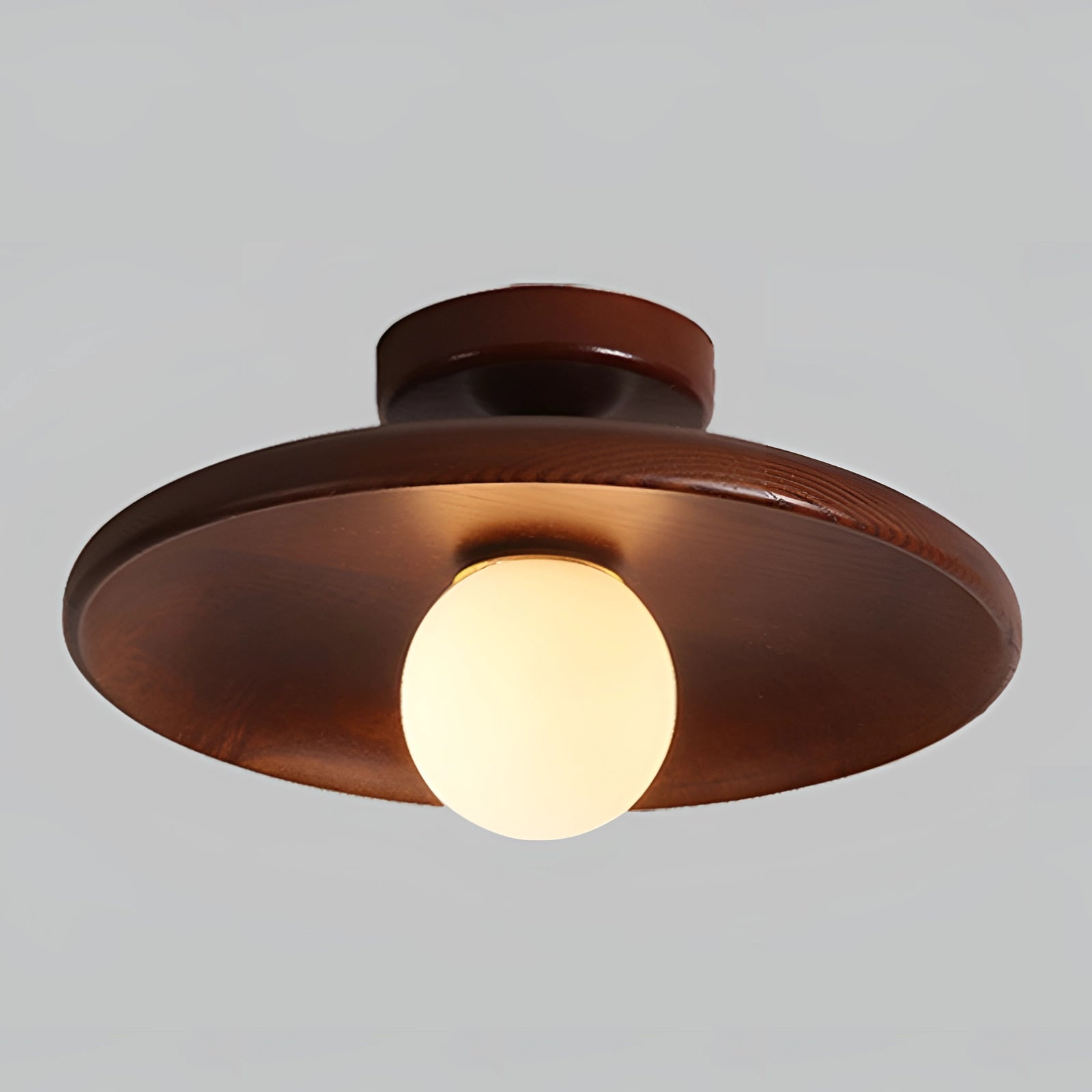 A modern bronze round flush mount ceiling light with a warm amber glow, featuring a circular design with metal and wood elements, suitable for home interiors.