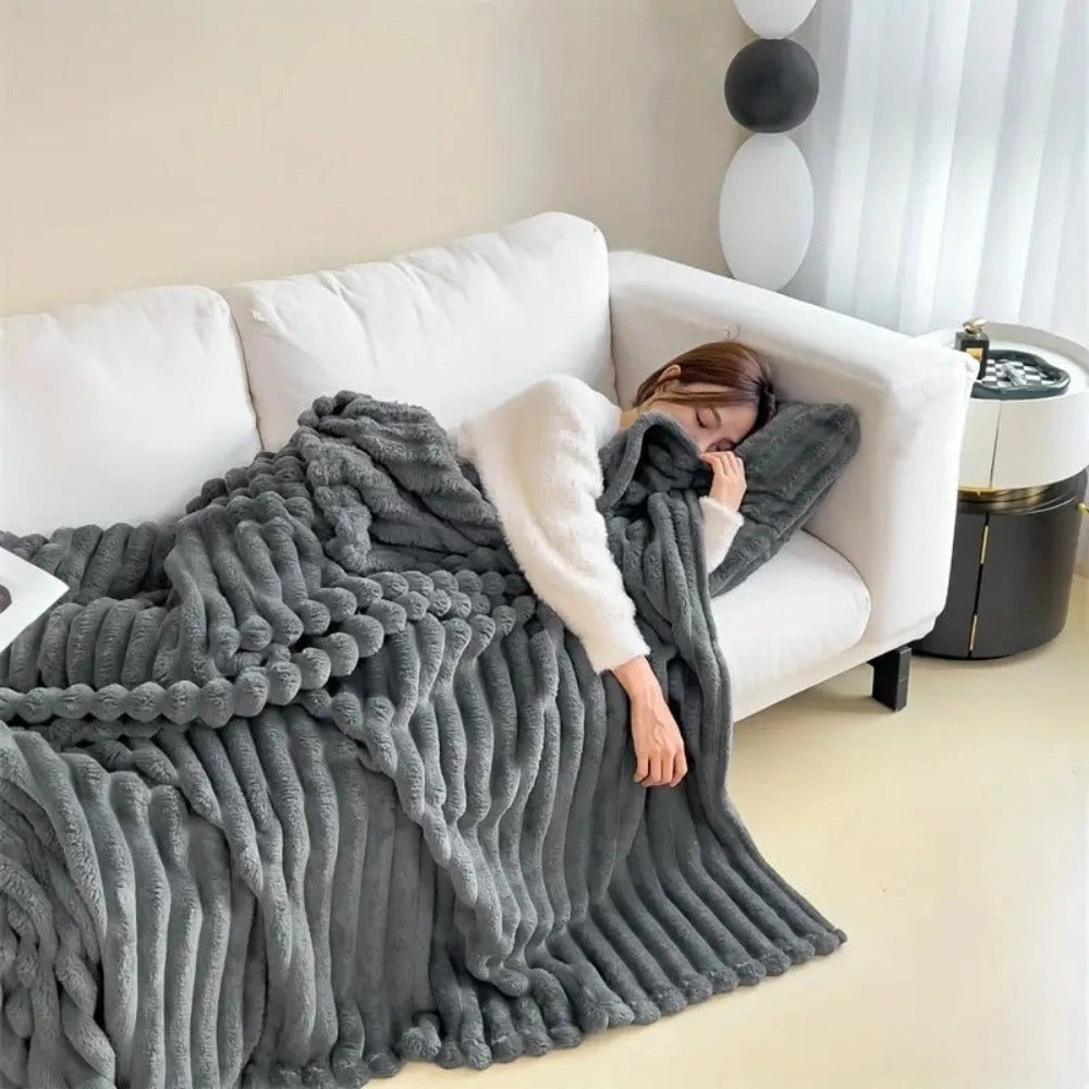 Chunky gray knit blanket draped over a cozy sofa, with a plush pillow nearby on a wooden floor.