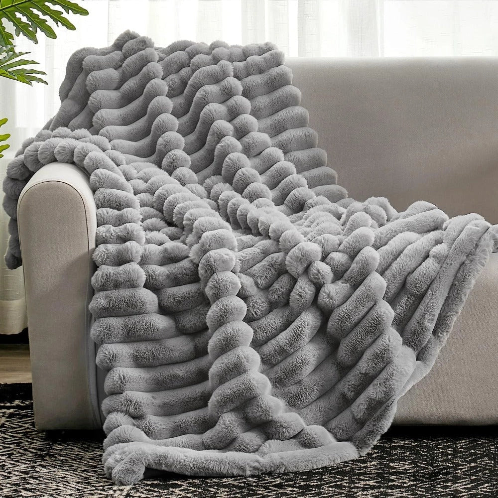 Cozy gray chunky knit blanket draped over a sofa, showcasing its thick, textured pattern and soft woolen material.