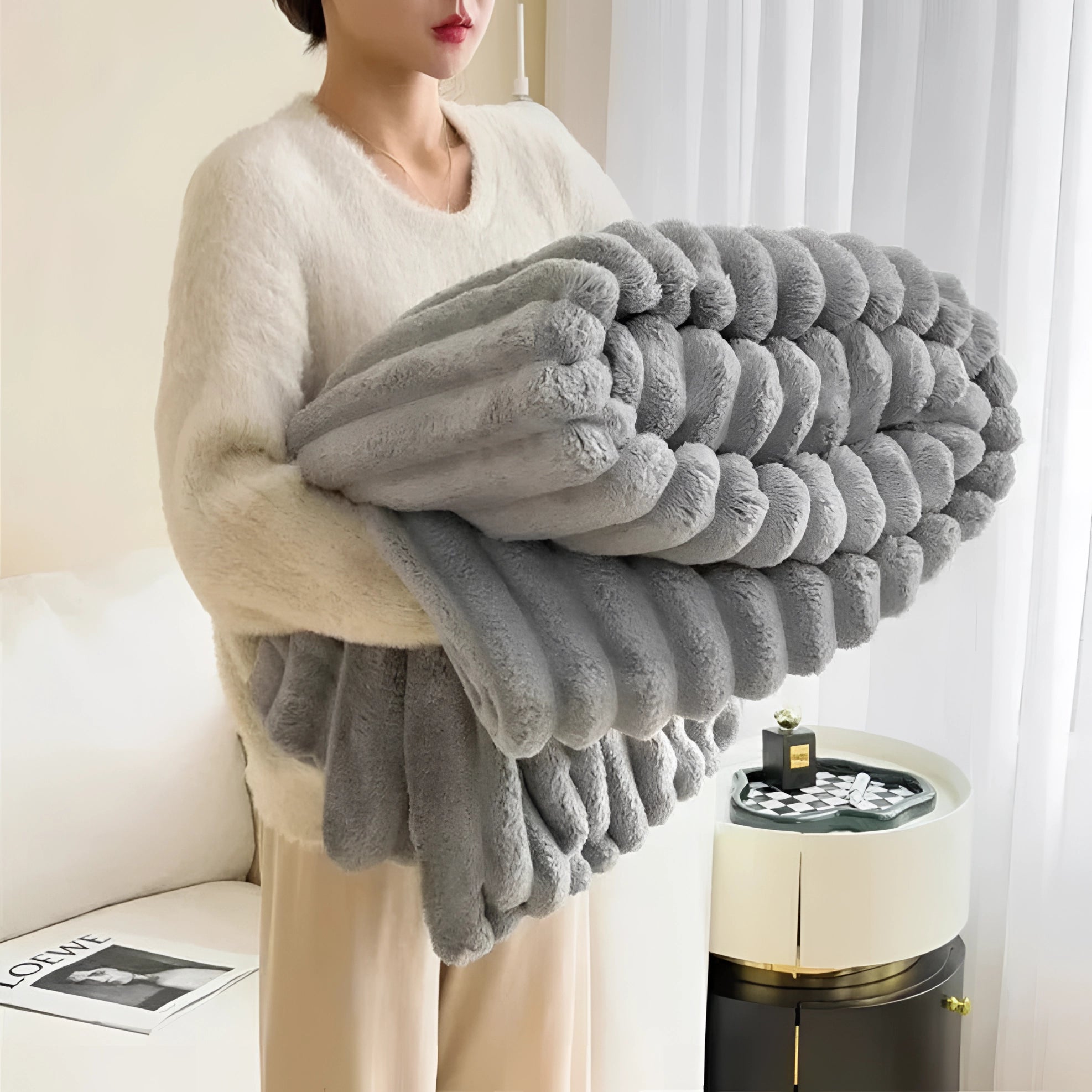 Chunky knit blanket in light grey draped over a cozy sofa, showcasing its thick, woolen texture and handmade design, with a soft and inviting appearance.