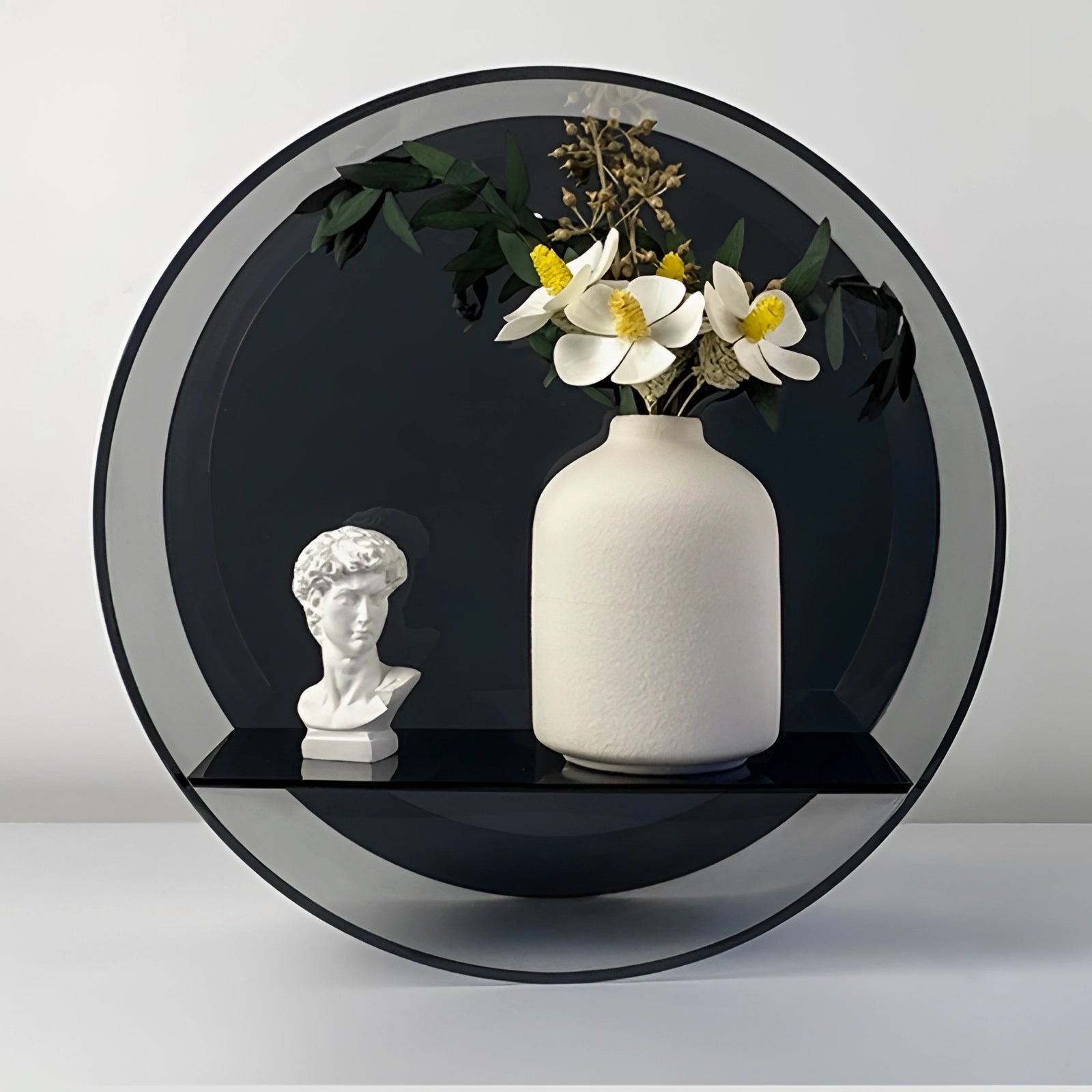 Circular black glass floating shelf adorned with modern minimalist decor, featuring a clear drinking glass with liquid, a small potted plant with green foliage, and a decorative flower with colorful petals.