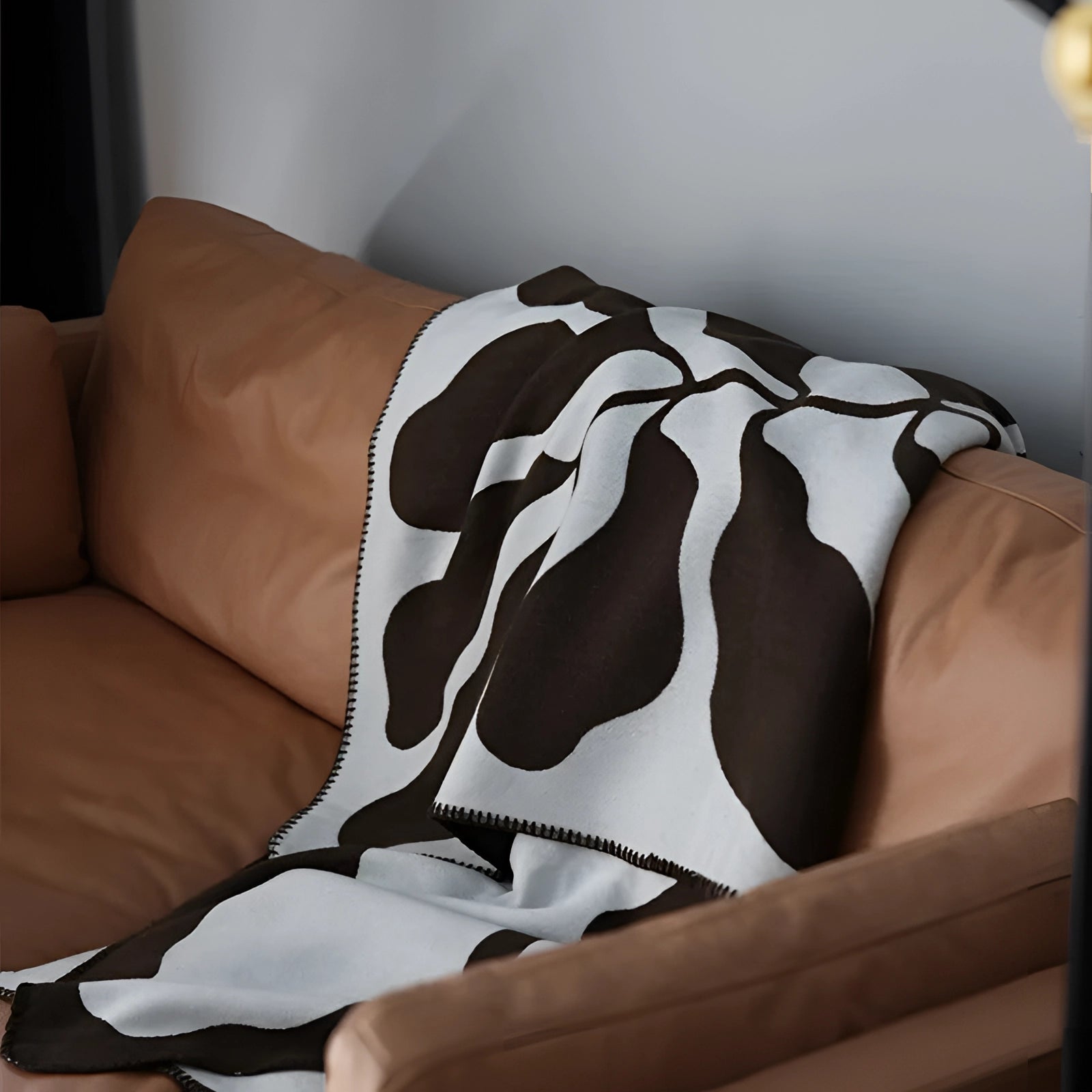 Brown and white cow print fleece throw blanket draped over a couch, showcasing an animal pattern design in a cozy interior setting, complemented by pillows and other linens.