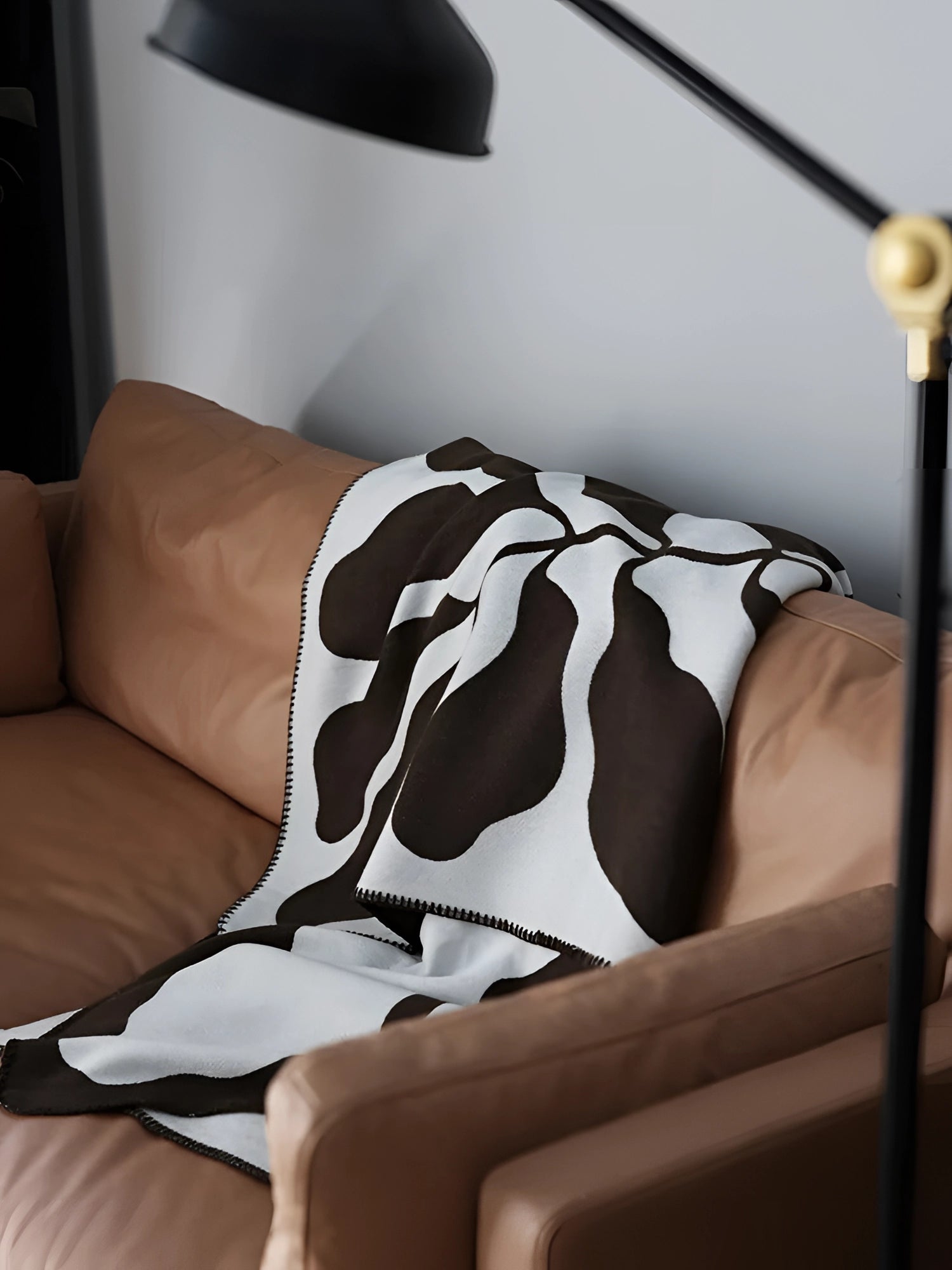 Brown and white cow print throw blanket draped over a light-colored couch in a cozy interior setting.