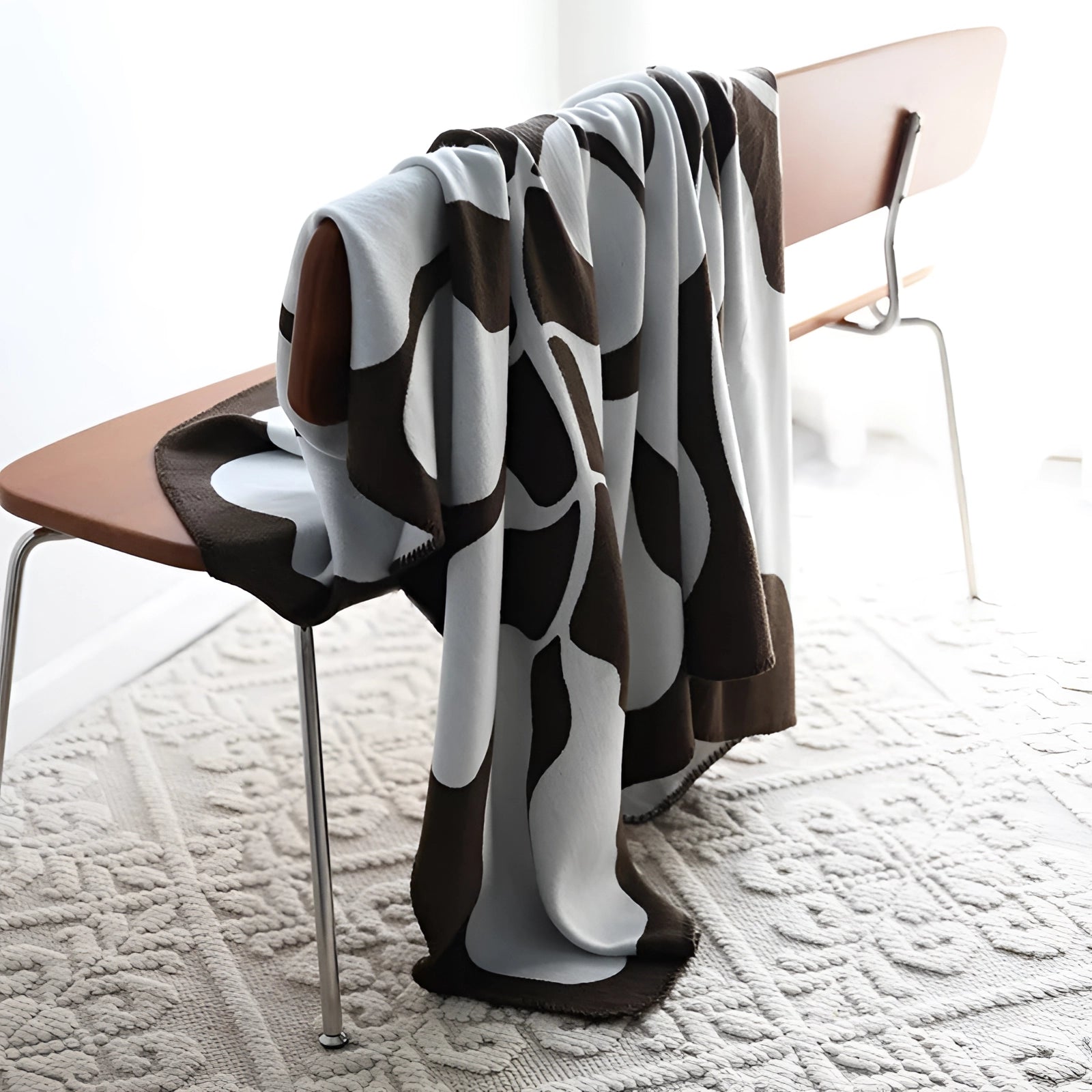 Brown and white cow print throw blanket draped over a chair in a cozy room setting with wooden flooring.