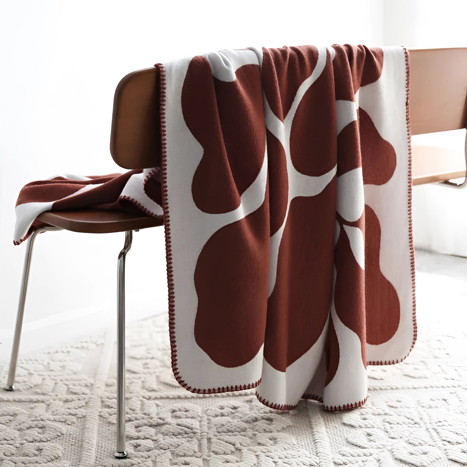 Brown and white cow print throw blanket draped over a wooden chair on a brick red floor.