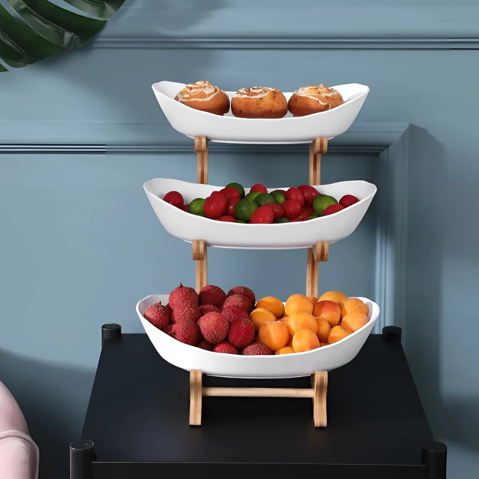 Double-decker ceramic snack bowl set with a bamboo stand placed on a table, filled with assorted natural foods including oranges.