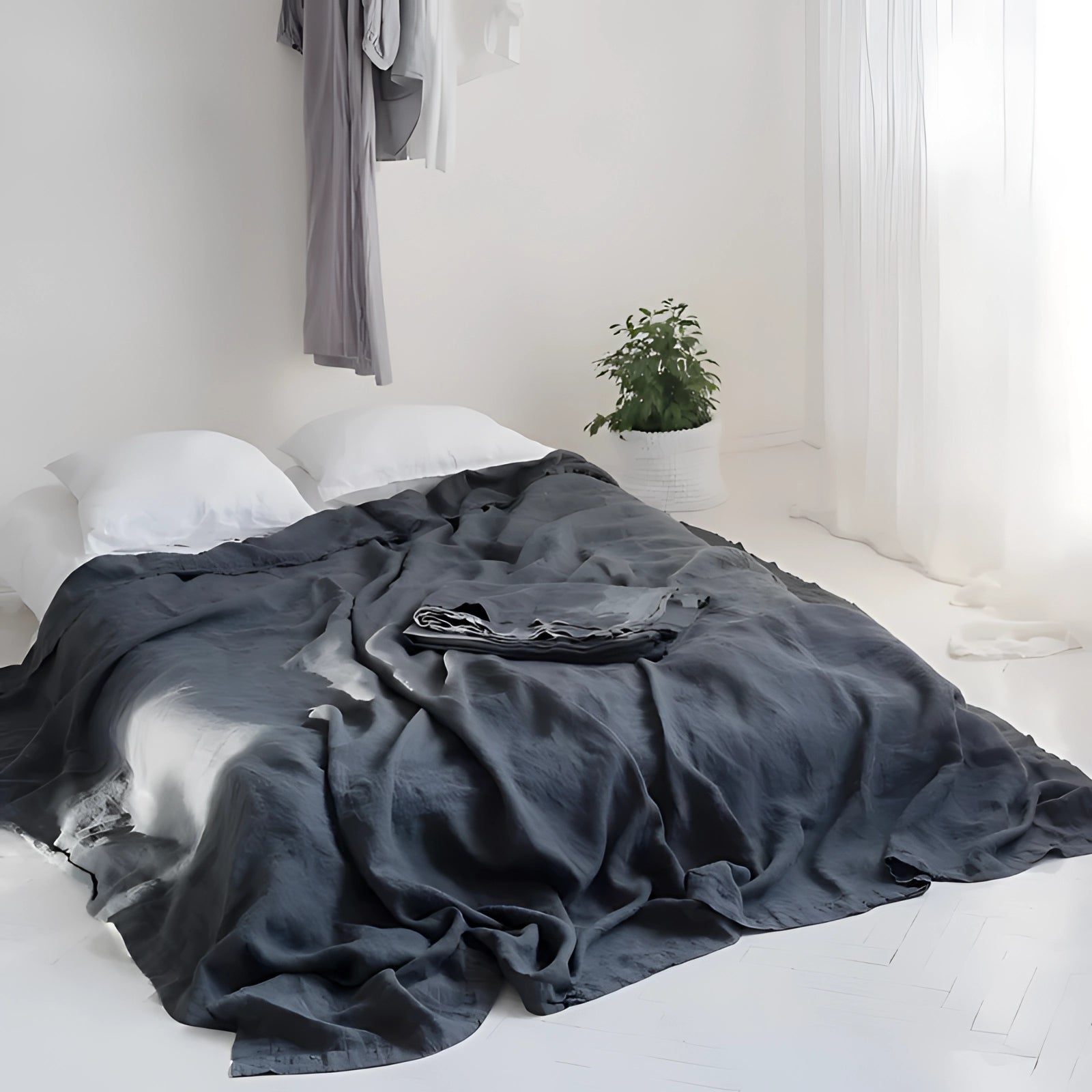 Black eco-friendly linen duvet cover in a bedroom setting, featuring organic and breathable bedding on a neatly made bed, with wooden flooring and a touch of greenery for added comfort and interior design appeal.