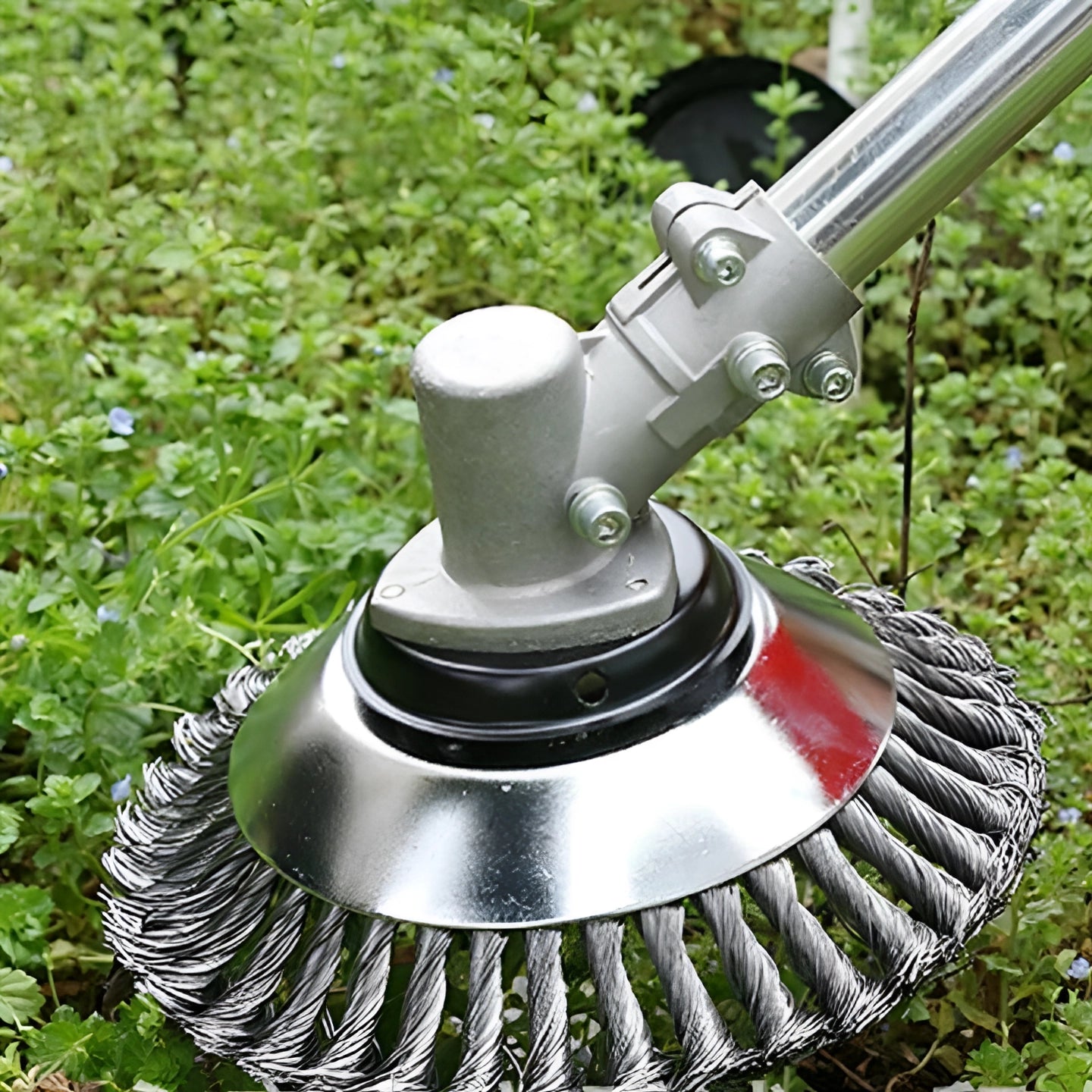 
A green and metal weeding brush featuring a circular design, suitable for removing weeds from grass and stone surfaces, with components resembling an automotive wheel system and bicycle handlebar.