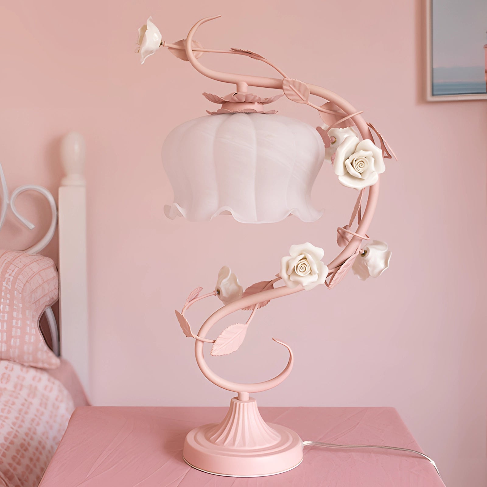 Elegant pink rose table lamp with a shabby chic floral vine design, featuring a pink lampshade and white wooden base, placed on a table.