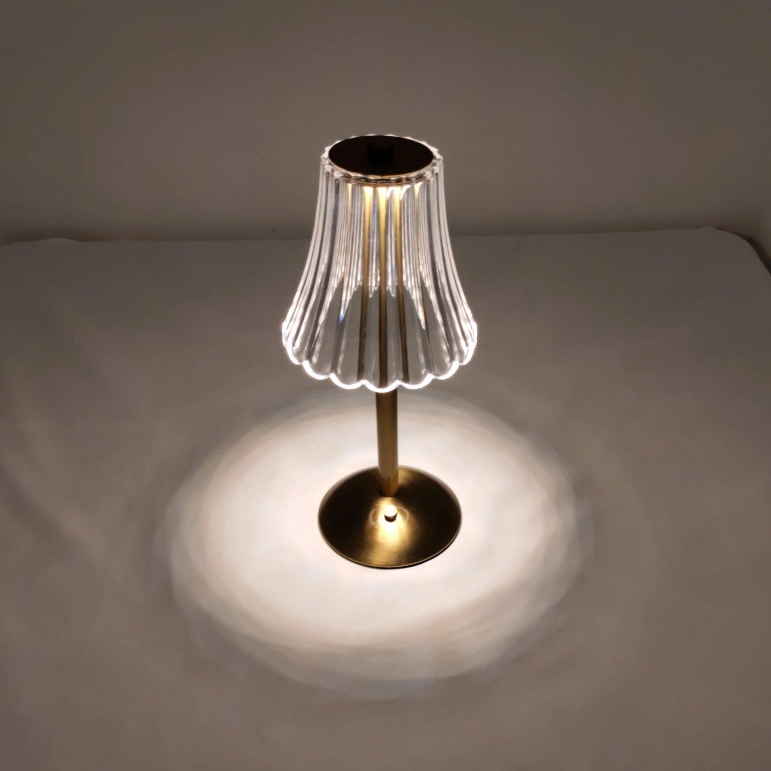 Elegant pleated table lamp with acrylic lampshade, modern gold base, and LED light on a wooden table.