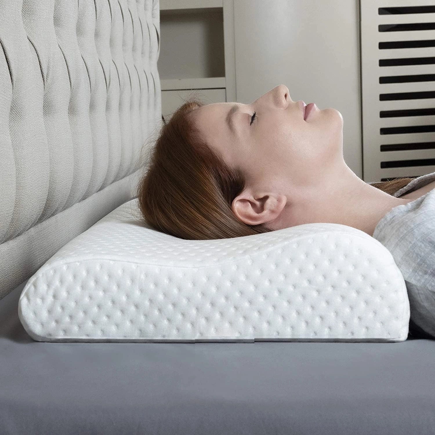 Ergonomic memory foam contour pillow designed for cervical and neck support, placed on a wooden flooring surface.