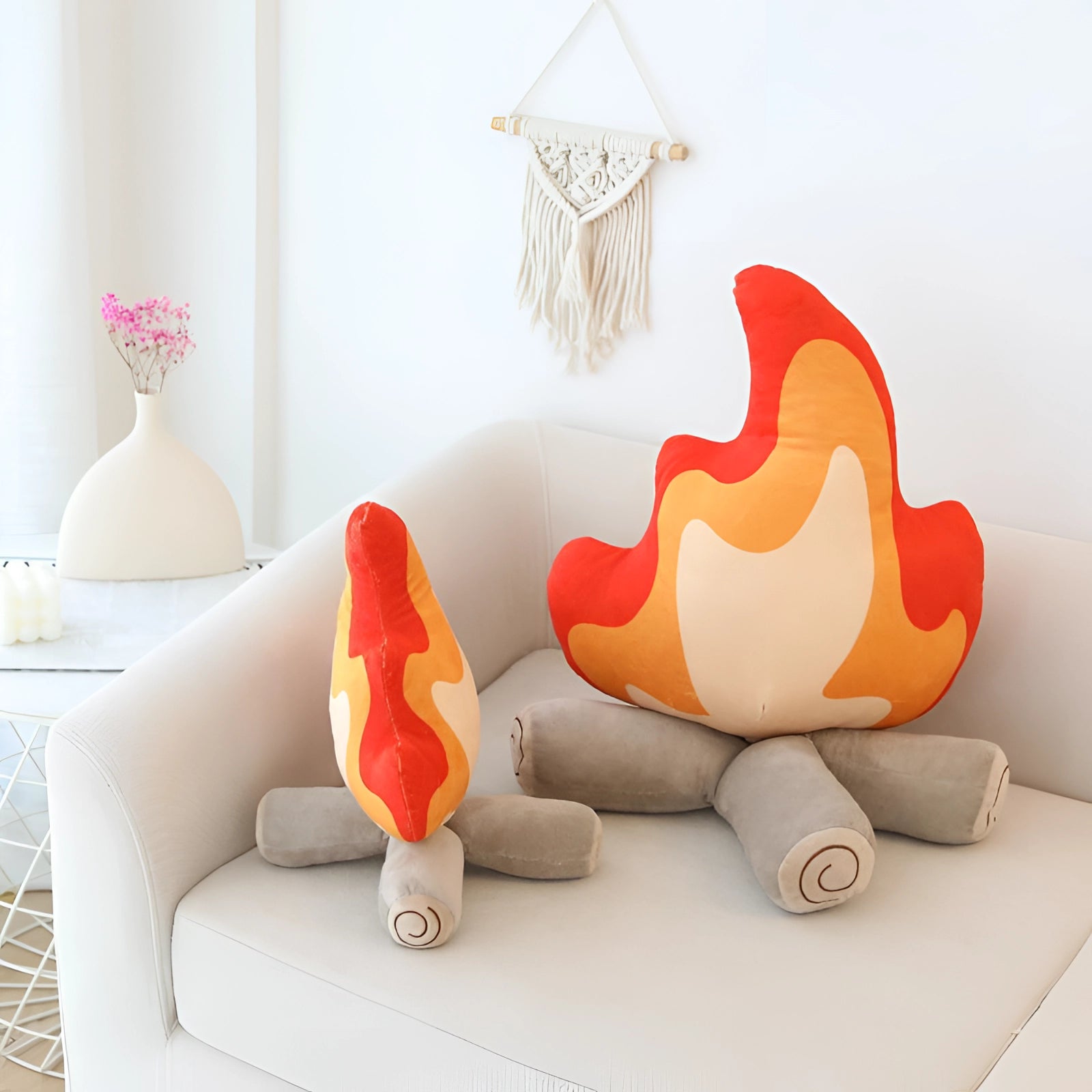 Flame-shaped plush pillow in vibrant orange placed on a modern couch, complementing the artistic interior design of a chic living room with a wooden lamp and stylish decor elements.