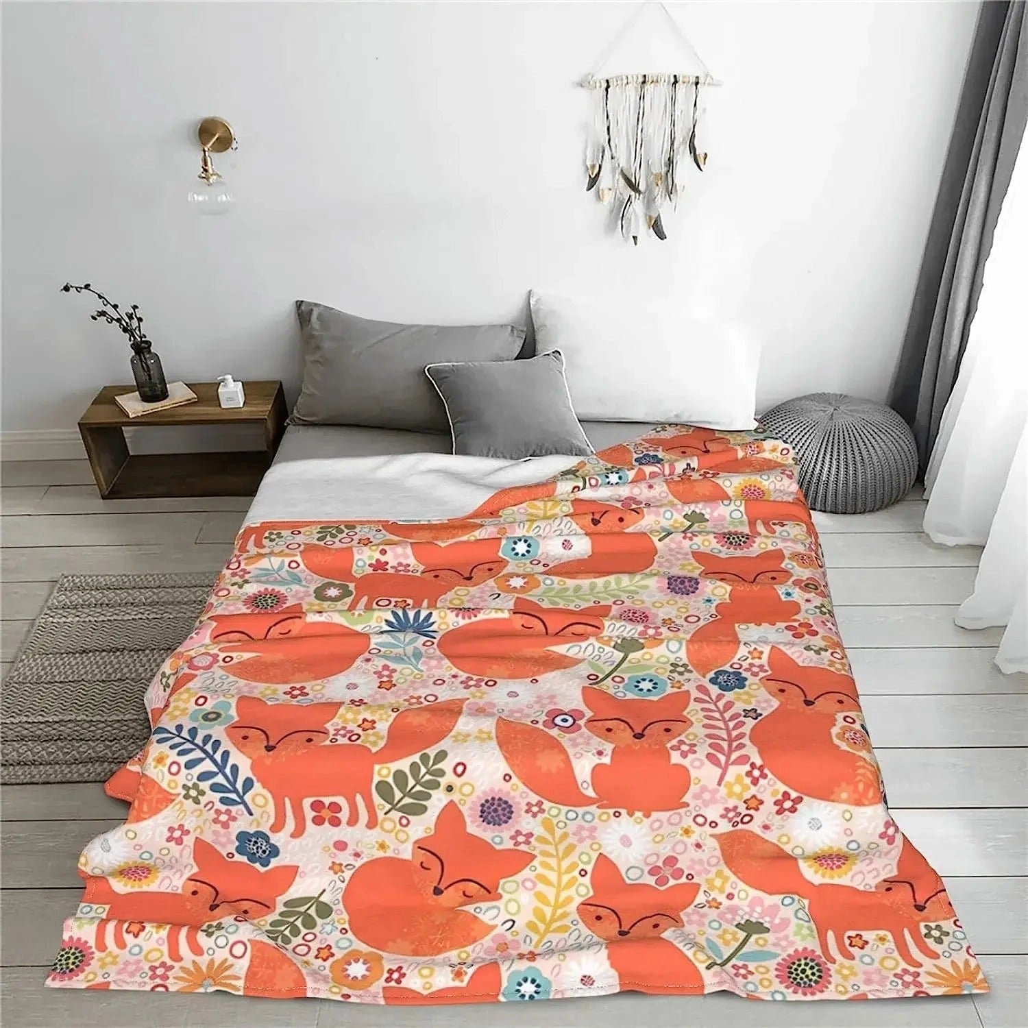 
A cozy fox print throw blanket featuring a cute woodland design in shades of orange and grey, draped over a bed in a warmly decorated interior with wooden furniture and grey flooring.