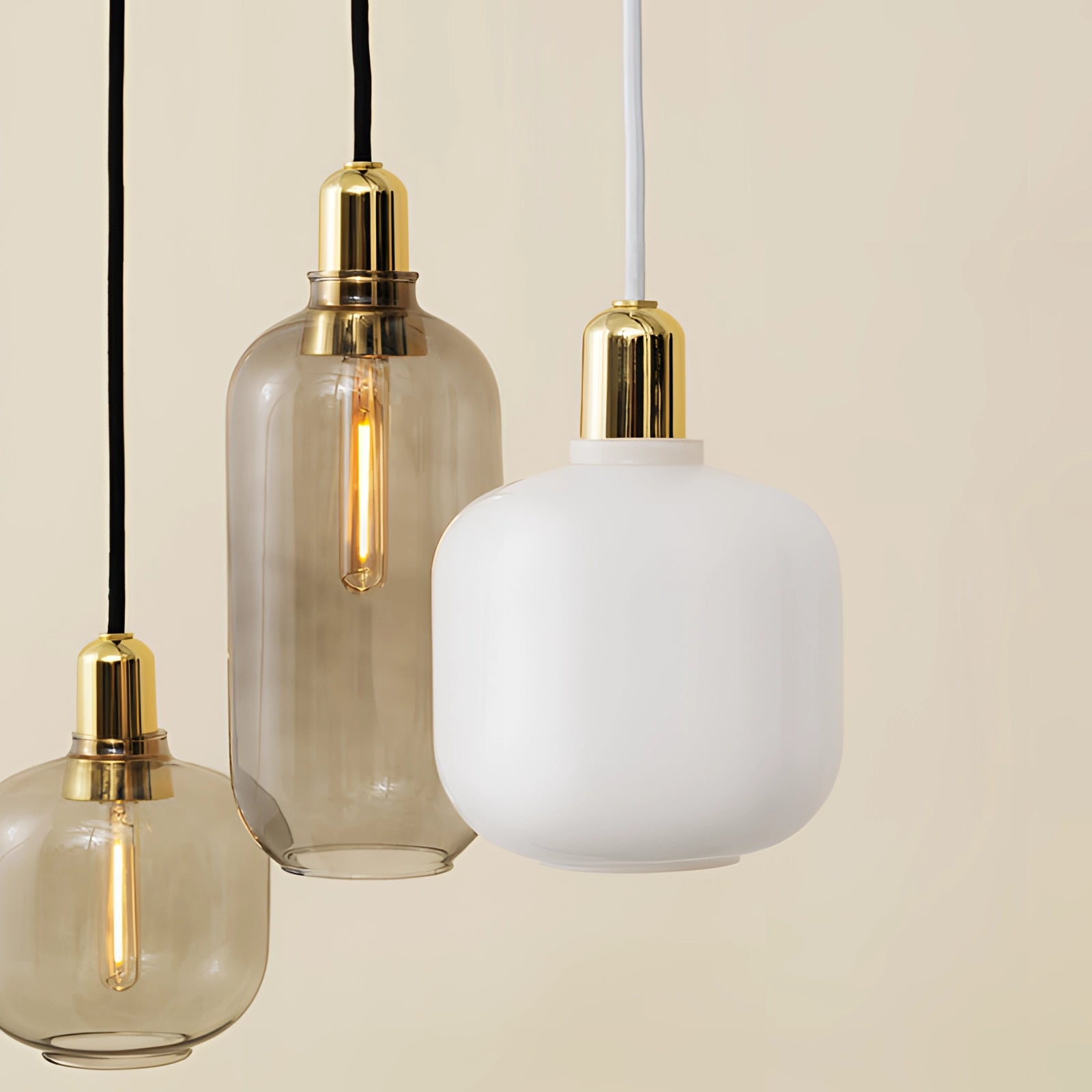 A Scandinavian minimalist pendant light featuring a frosted glass shade and brass accents, with a warm amber hue, suspended from a ceiling.