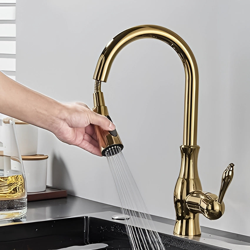 Gold brass kitchen faucet with a high-arc, modern design and a pull-down spray feature, installed above a kitchen sink with a visible countertop and cabinetry in the background.