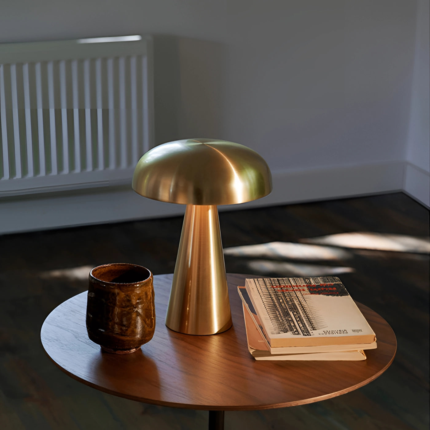 A sleek modern gold mushroom table lamp with a brushed metallic finish, placed on a wooden desk in a stylish interior setting.