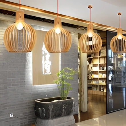 Golden wooden pendant light hanging from the ceiling, illuminating a modern dining room with wooden floors and a backdrop of houseplants and decorative elements.