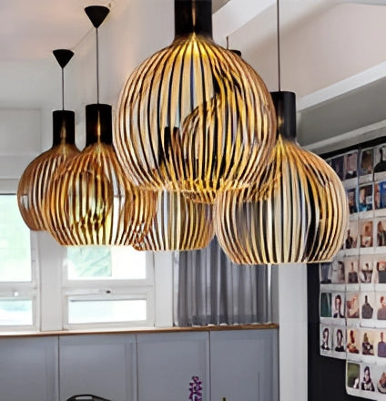 Golden wooden pendant light fixture with a modern design, featuring an orange hue and textile accents, hanging in a stylish dining room interior with a window and shelving.