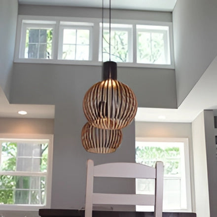 Golden wooden pendant light with a modern design hanging in a dining room, featuring a rectangular wooden shade and casting warm light, complementing the contemporary interior decor.