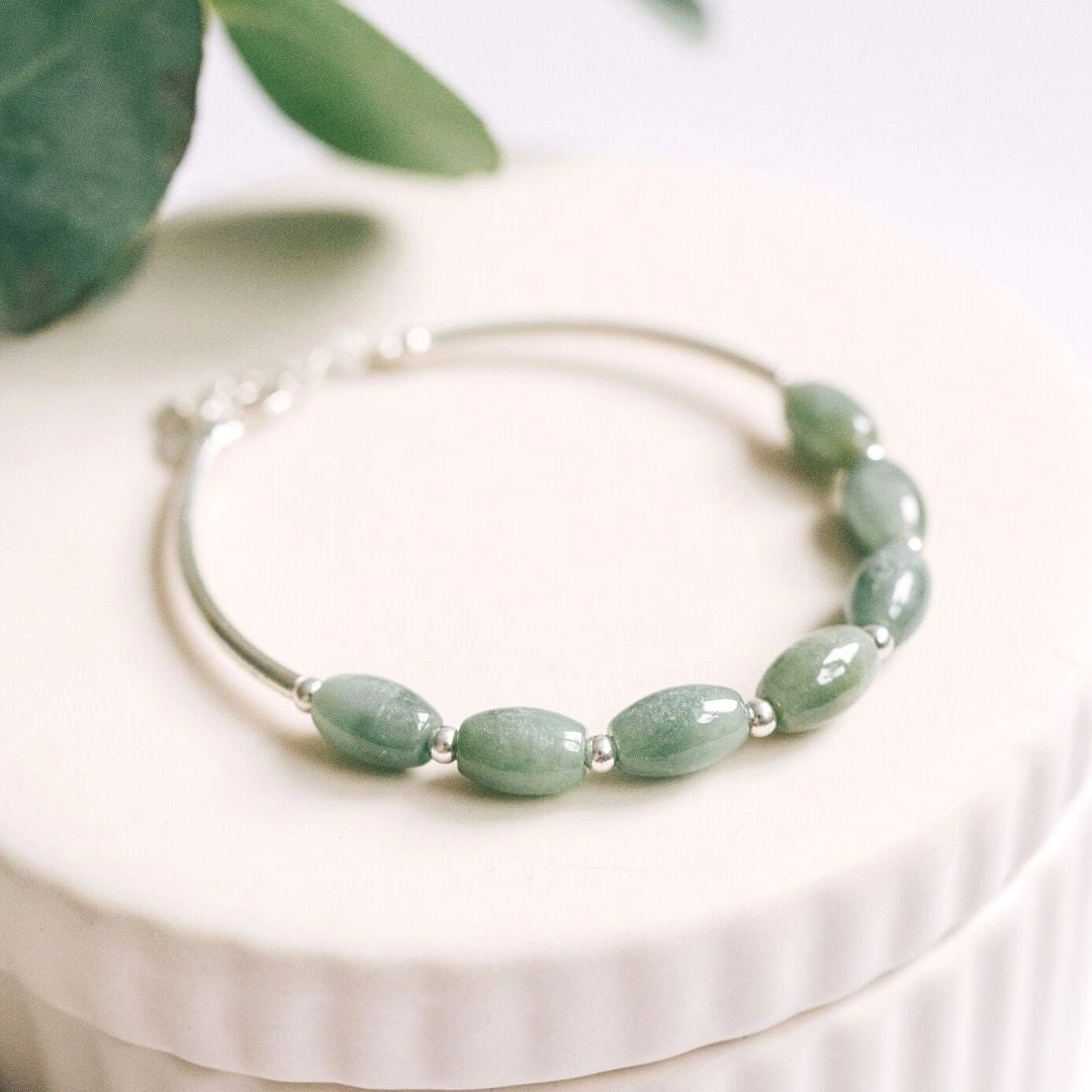 A silver bracelet featuring an oval-shaped green jade stone, showcasing a natural and artistic jewelry design.