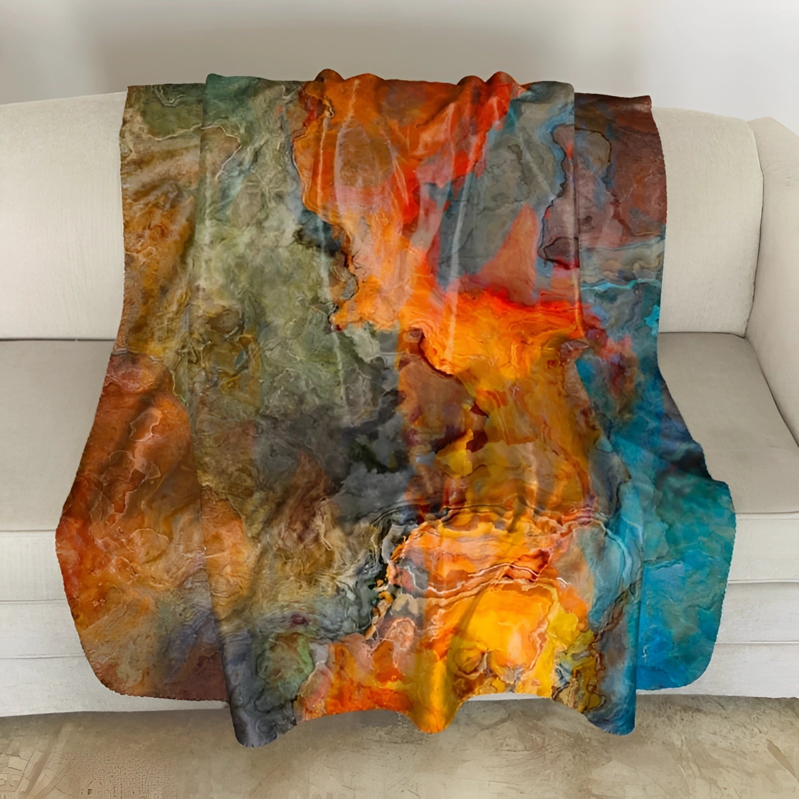 Hand-painted luxury silk throw blanket with vibrant artistic design, draped over a studio couch with a predominantly orange color palette, enhancing the home's artistic decor.