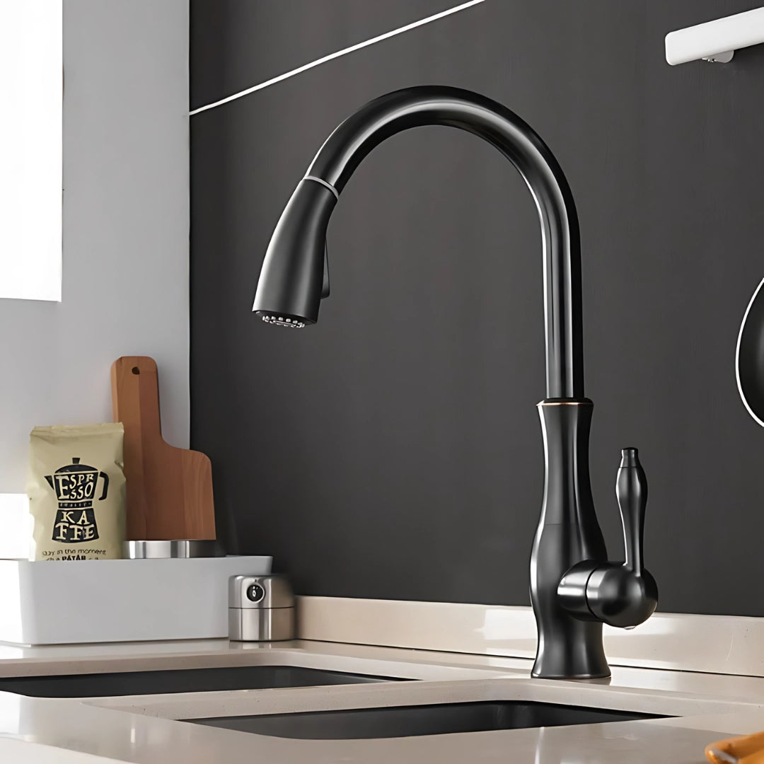 
Black high-arc stainless steel pull-down kitchen faucet with a modern design, installed over a grey sink, with surrounding interior decor including a plant and light-colored walls.