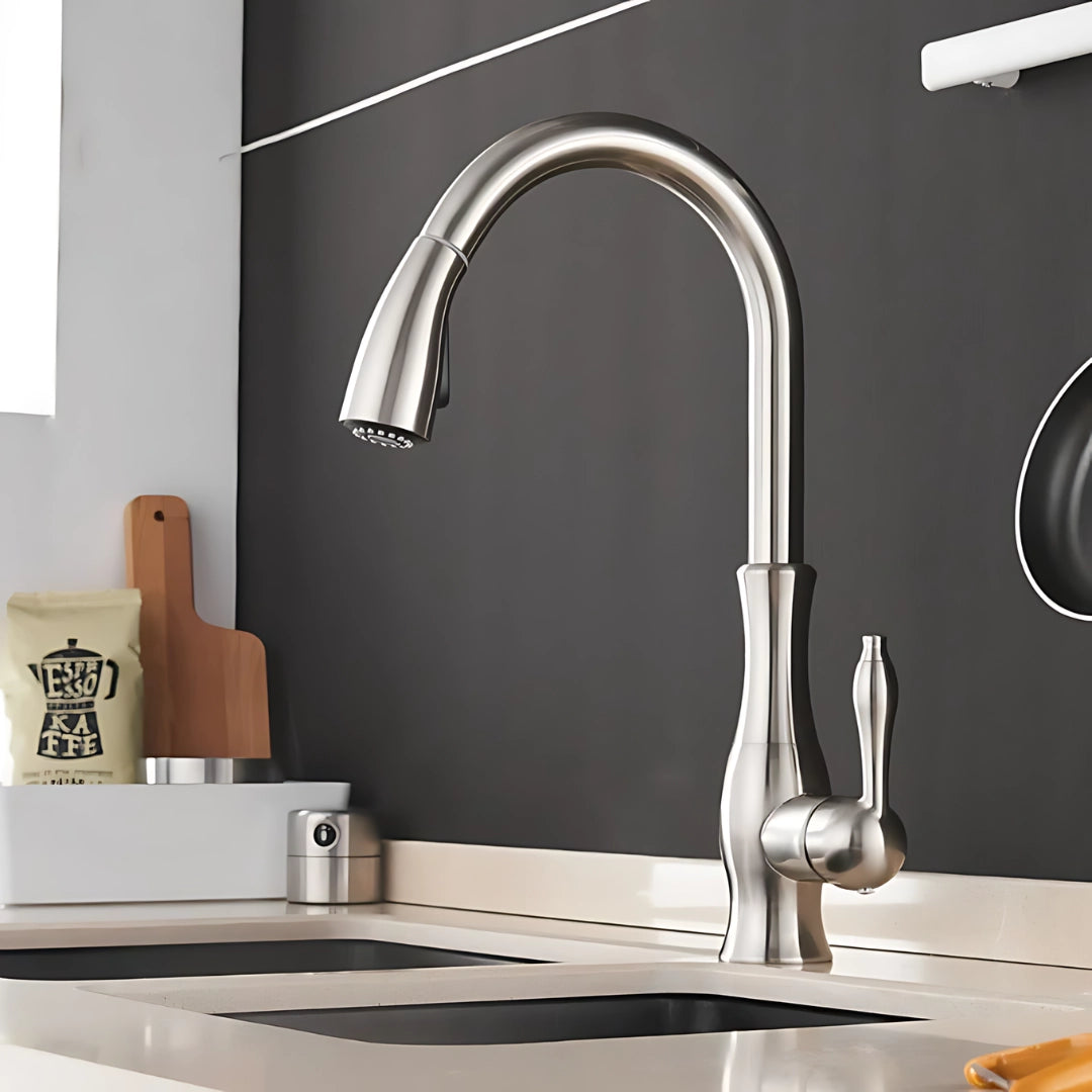 A modern chrome high-arc stainless steel pull-down kitchen faucet installed on a countertop, with a sleek design featuring a single lever handle. The faucet is set in a stylish kitchen interior, complemented by a potted plant and white walls.