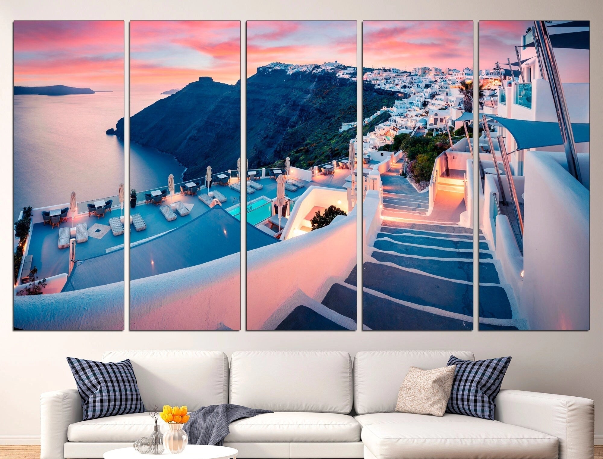 Large Santorini canvas print displayed in a living room setting with a 5-panel design measuring 101"x57". The artwork features a vibrant blue and orange color scheme, complementing the azure and orange elements in the room's interior design. The canvas is hung above a couch, enhancing the room's aesthetic with a Greek-inspired wall décor art.