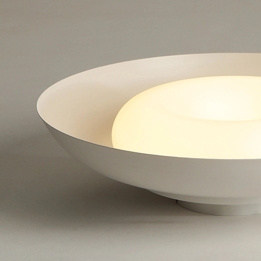 Modern minimalist LED ceiling light with a round panel design, flush mounted to a ceiling, emitting a soft-white glow.