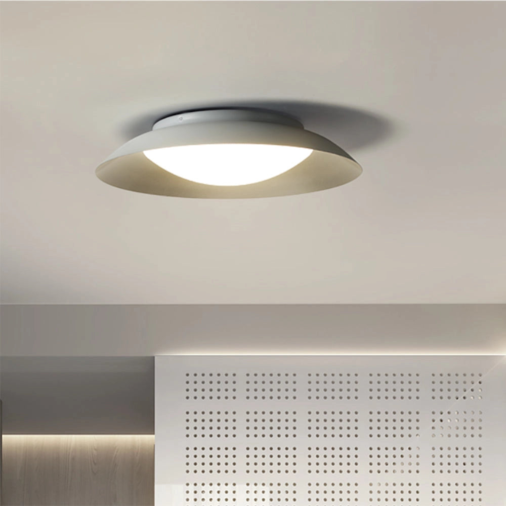 Modern minimalist round LED ceiling light with a soft-white flush mount design, featuring a circular panel with metallic and composite material elements, installed on a wooden ceiling.