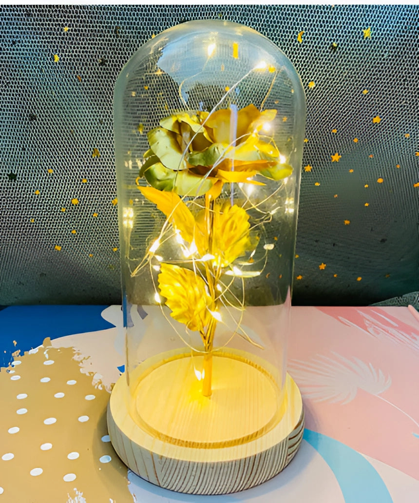 LED rose dome featuring a new 24-karat gold enchanted rose with fairy lights, encased in a clear glass dome on a wooden base, serving as a decorative piece for table or home decor.