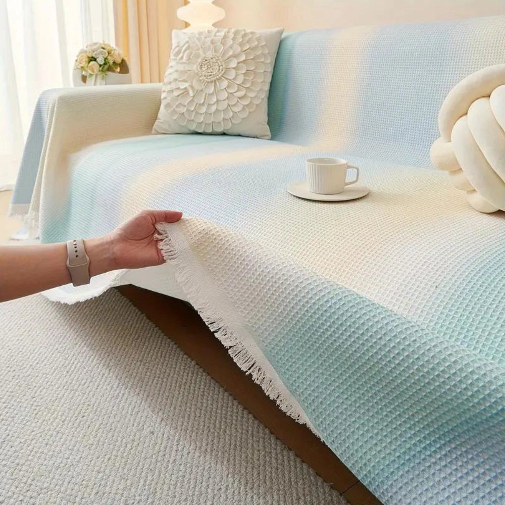 Lightweight pastel blue bedspread made of textured cotton with fringed edges, draped over a wooden table or bed in a cozy, well-designed interior setting.